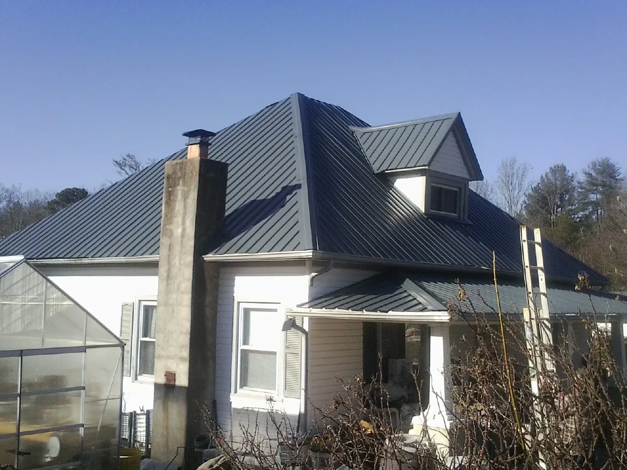 Dark blue standing seam metal roof on a white farmhouse with dormer — Slate & Tile Roof Repair by Roofing Brothers in Ford Cliff