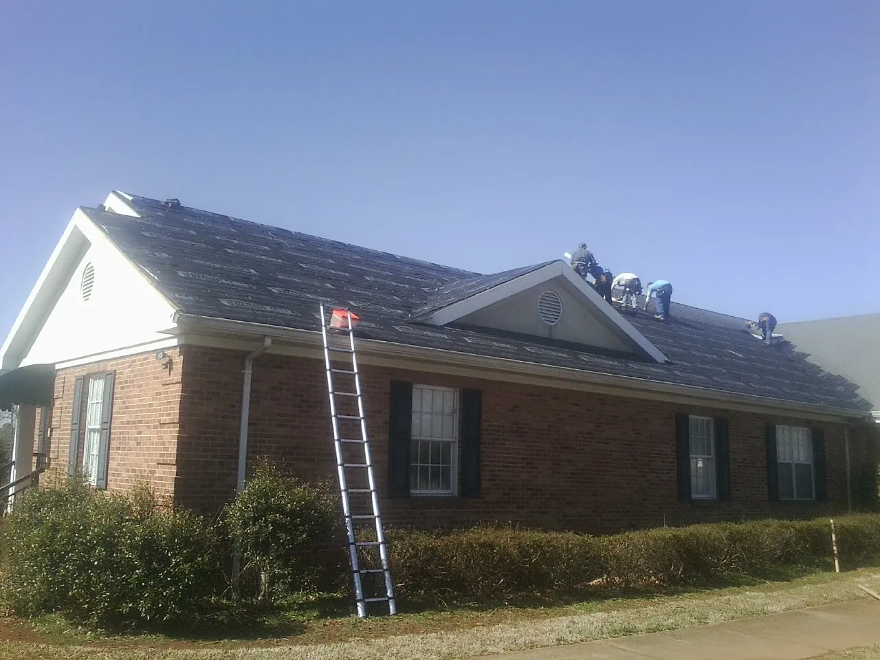 Crew tearing shingles off a brick ranch roof with a ladder set — Metal Roof Repair work by our crew in Ford Cliff