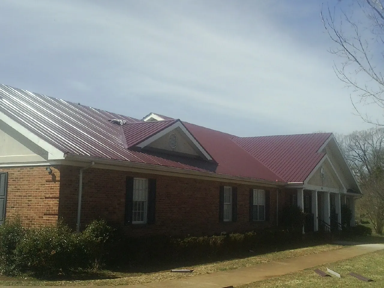 Red metal roof with gabled entries on a long brick building, from a Hail Damage Roof Repair job in Ford Cliff
