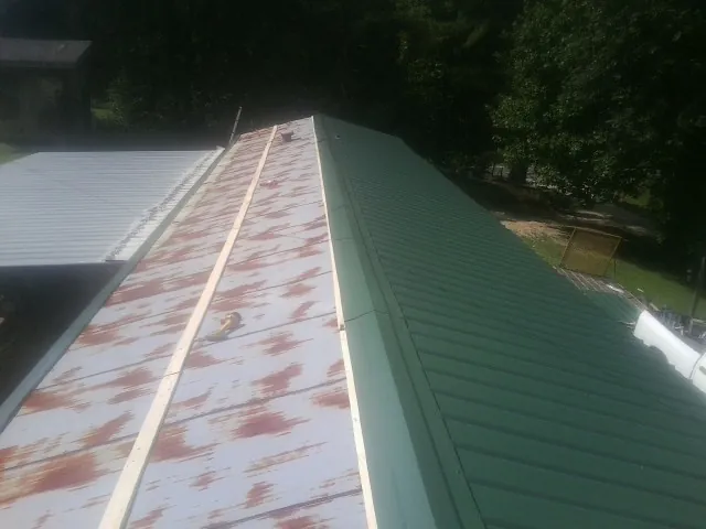 Old rusted panels beside newly installed green metal roofing — Wind Damage Roof Repair by Roofing Brothers in Ford Cliff