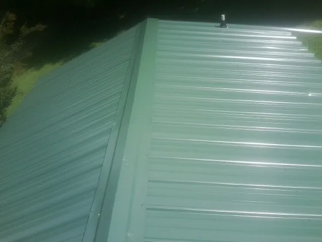 New green metal panels meeting at the ridge of a roof — Flat Roof Repair work by our crew in Ford Cliff