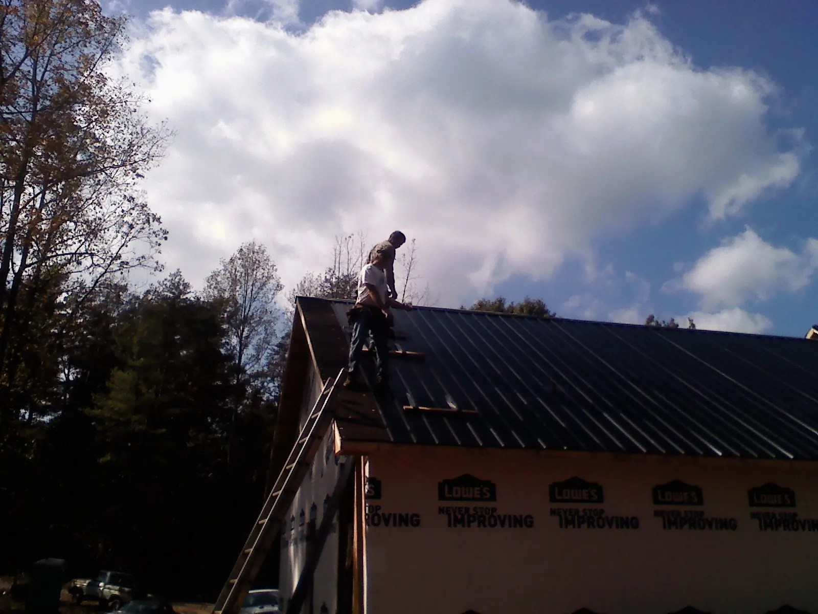 Roofer fastening dark metal panels high against a cloudy sky, from a Roof Inspection job in Ford Cliff