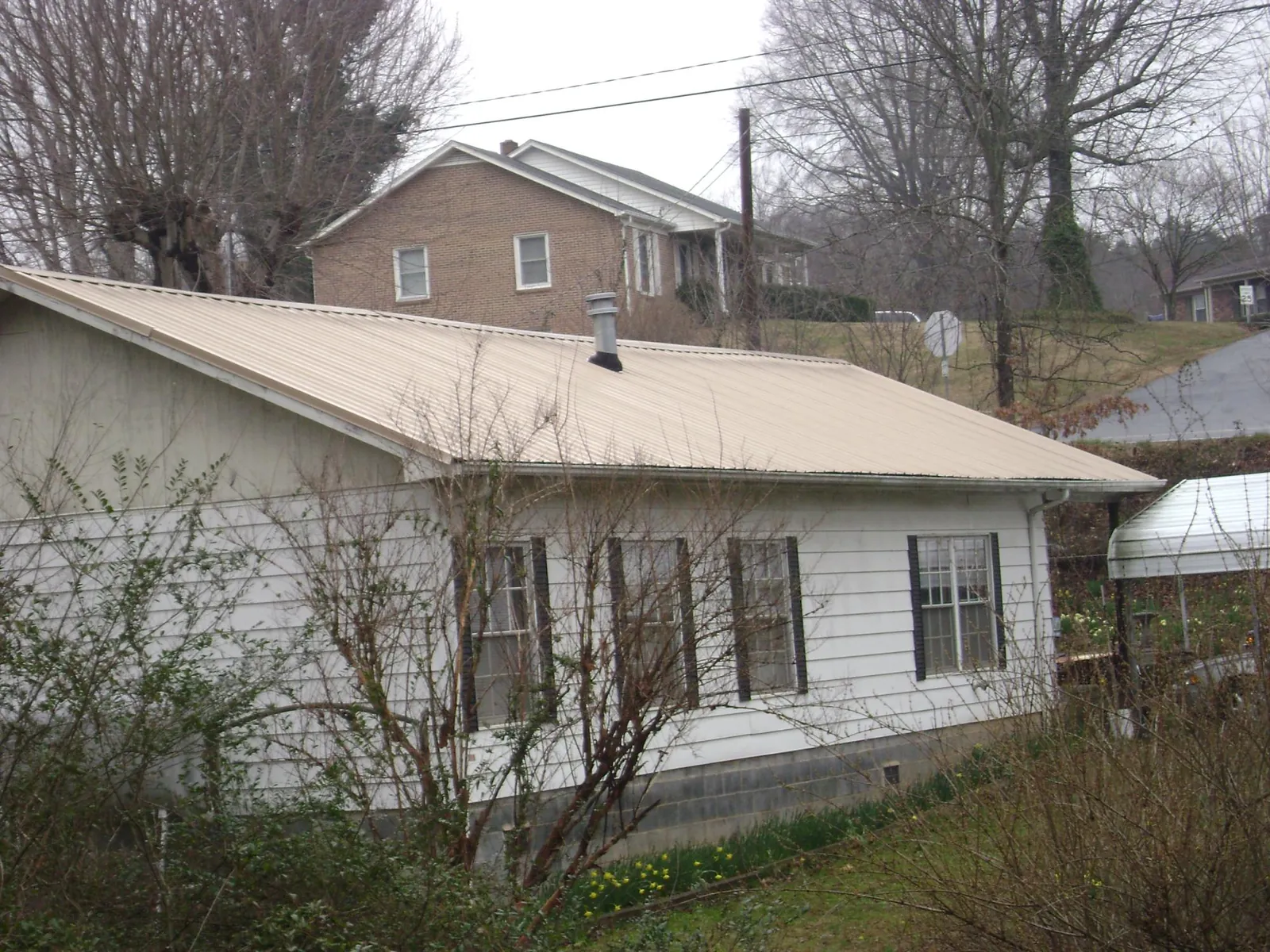 Tan metal roof on a white sided house set into a hillside — Commercial Roofing by Roofing Brothers in Ford Cliff