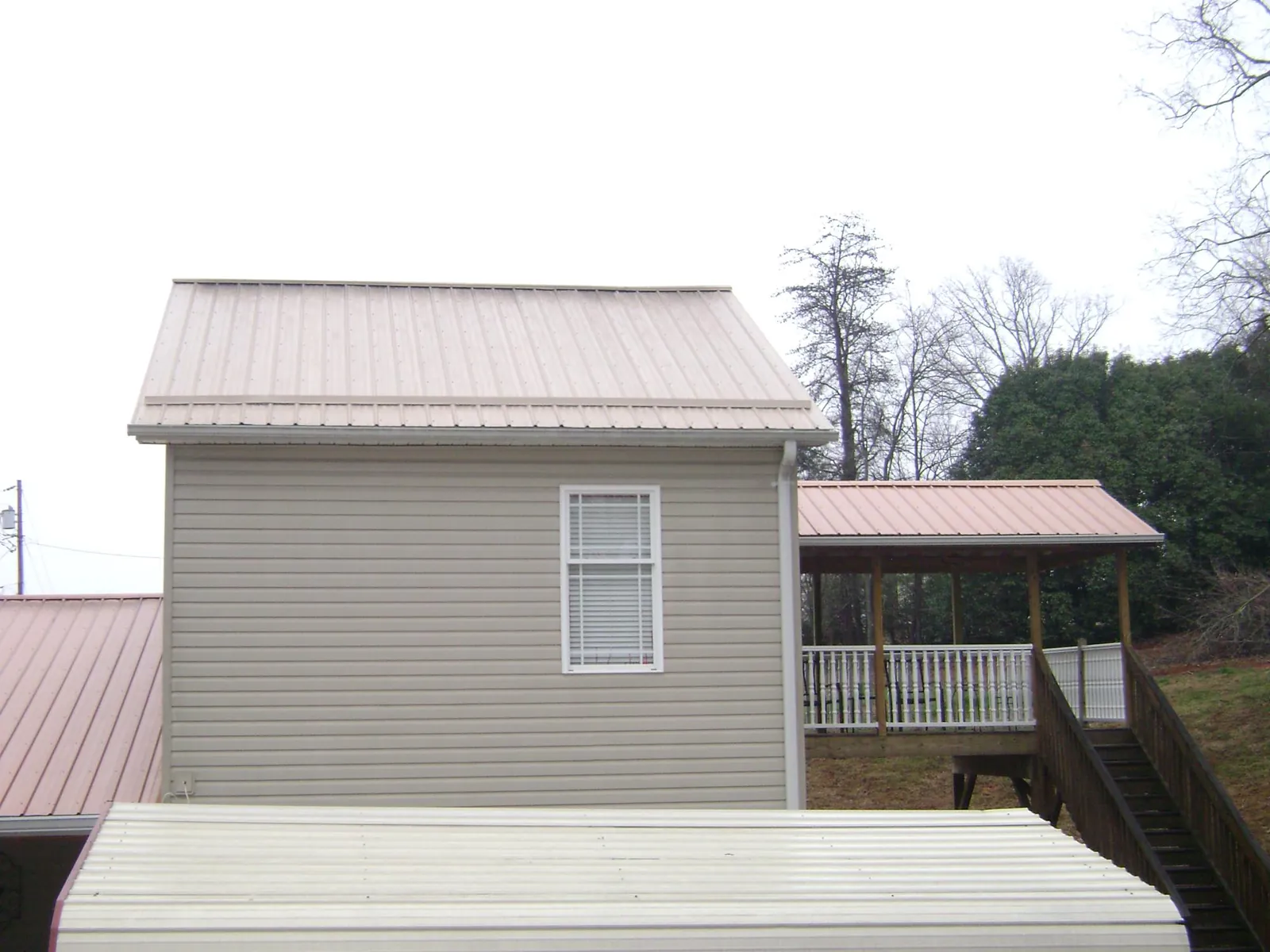 Tan metal roofs on a two story addition and attached porch, from a Roof Replacement job in Ford Cliff